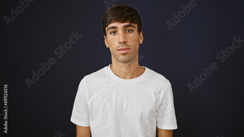 Portrait of a handsome young hispanic man with a serious expression, standing isolated against a black background, concentrated, looking away from the camera, radiating a relaxed confidence. photo