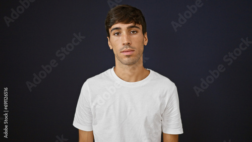 Obraz na plátně Portrait of a handsome young hispanic man with a serious expression, standing isolated against a black background, concentrated, looking away from the camera, radiating a relaxed confidence