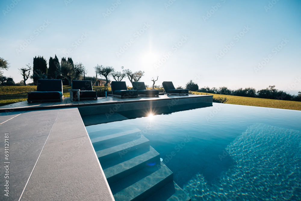 Modern pool with blue water at a luxurious house with deck chairs, trees, and grass in the background