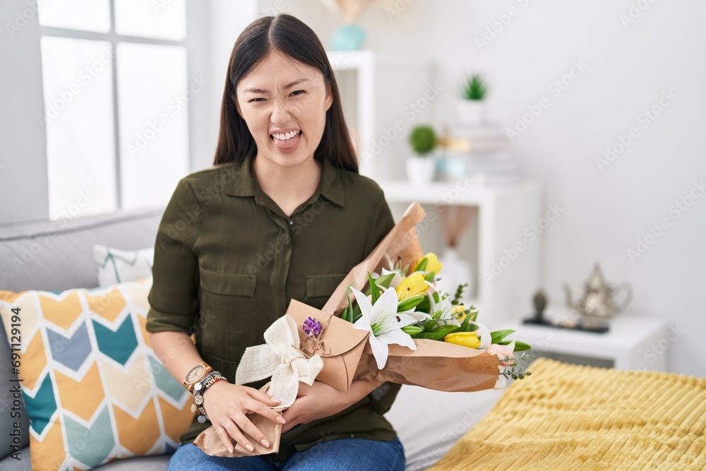 Φωτογραφία Chinese young woman holding bouquet of white flowers sticking tongue out happy with funny expression