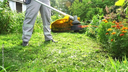 a man mows the grass with a grass trimmer photo