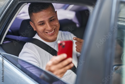 Young hispanic man doing video call with smartphone in the car smiling happy pointing with hand and finger © Krakenimages.com