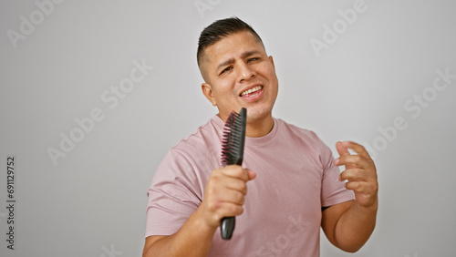 Handsome young latin man joyfully singing his heart out, using a brush as his microphone, isolated on a white background