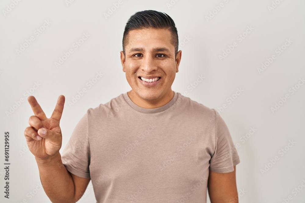 Hispanic young man standing over white background showing and pointing up with fingers number two while smiling confident and happy. Hispanic young man standing over white background showing and pointing up with fingers number two while smiling confident and happy.