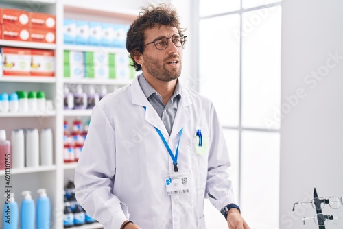 Young hispanic man pharmacist speaking at pharmacy