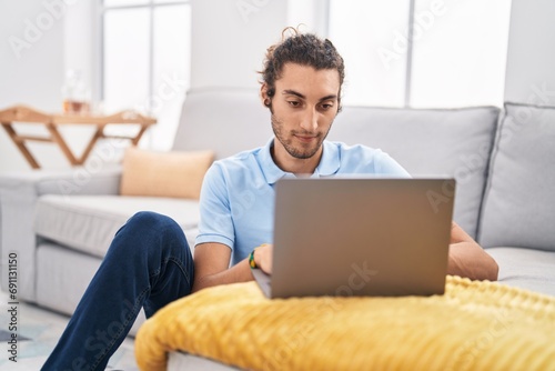 Young hispanic man using laptop sitting on floor at home photo
