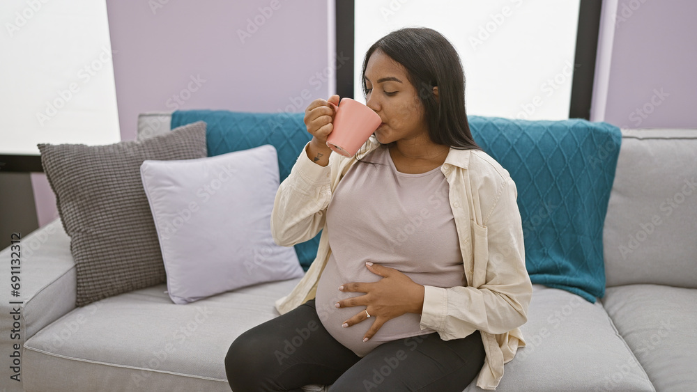 Home comfort, young pregnant woman enjoying a relaxing morning at home, drinking coffee and touching her belly on a comfortable sofa Home comfort, young pregnant woman enjoying a relaxing morning at home, drinking coffee and touching her belly on a comfortable sofa