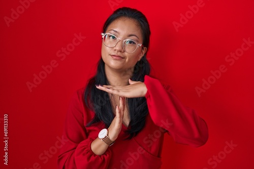 Asian young woman standing over red background doing time out gesture with hands, frustrated and serious face