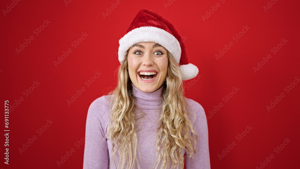 Young blonde woman smiling confident wearing christmas hat over isolated red background