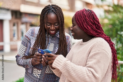 African american women friends using smartphone and credit card at street