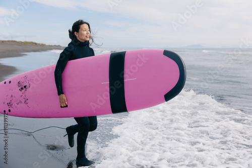 Happy surfer woman in wetsuit with surfboard go to winter surfing in ocean. Adventure Extreme travel sport concept