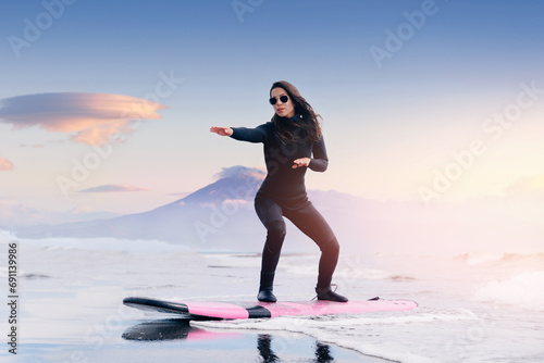 Extreme surfer woman in wetsuit with surfboard go to winter surfing in Atlantic ocean Kamchatka Russia. Adventure travel sport concept