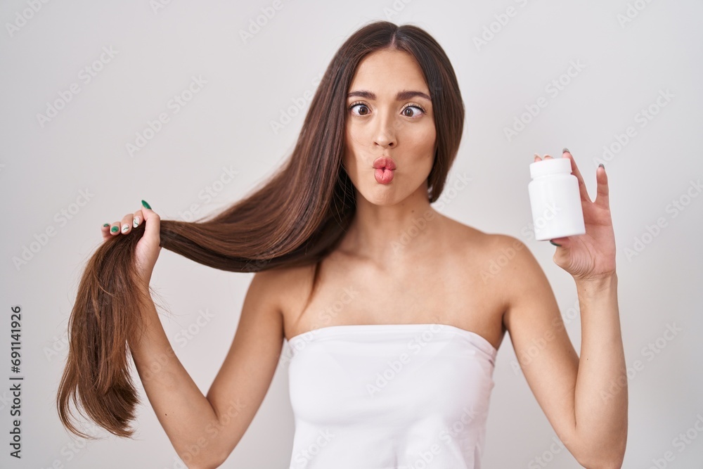 Young hispanic woman holding hair with hand and pills making fish face with mouth and squinting eyes, crazy and comical. Young hispanic woman holding hair with hand and pills making fish face with mouth and squinting eyes, crazy and comical.
