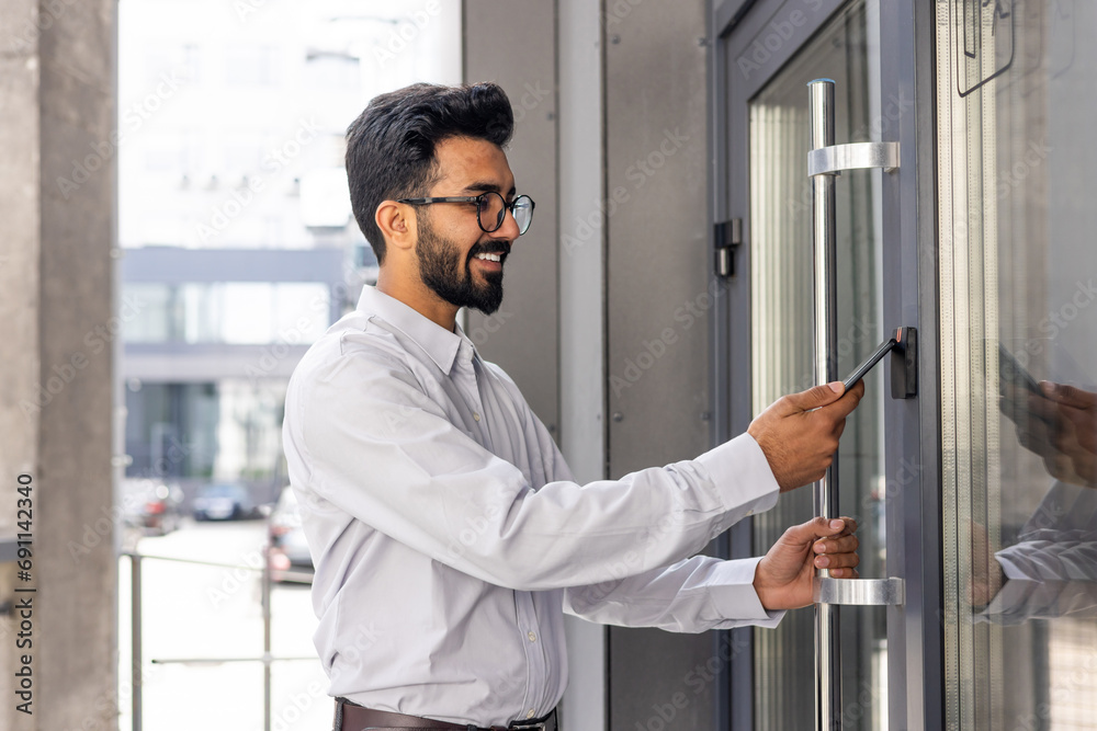 © Liubomir - Young businessman using phone to open office door of building, man happy using wireless access, businessman going to work happy smiling.
