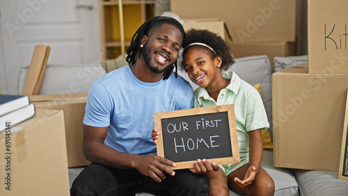African american father and daughter holding blackboard sitting on sofa at new home