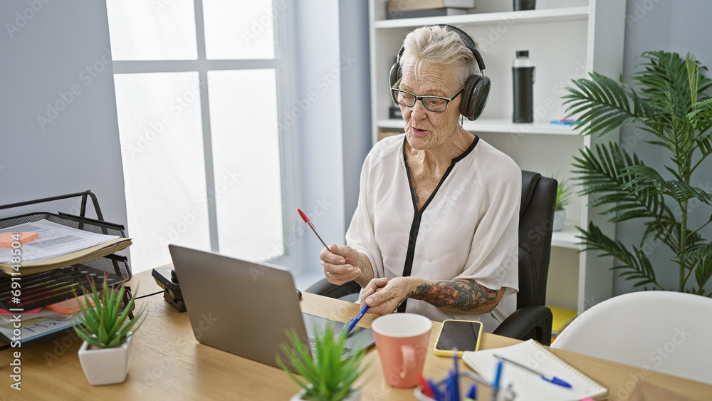 Jovial senior grey-haired business woman tapping into the rhythm at work, gleefully drumming her desk, enjoying music in office Jovial senior grey-haired business woman tapping into the rhythm at work, gleefully drumming her desk, enjoying music in office