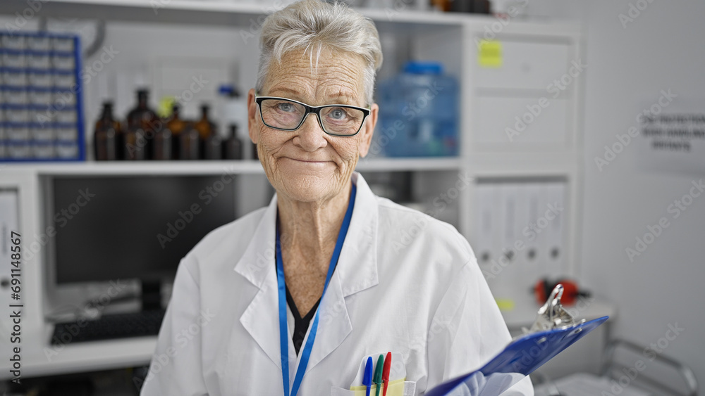 Senior woman scientist with grey-hair confidently smiling at a lab, while holding a checklist for medical research.