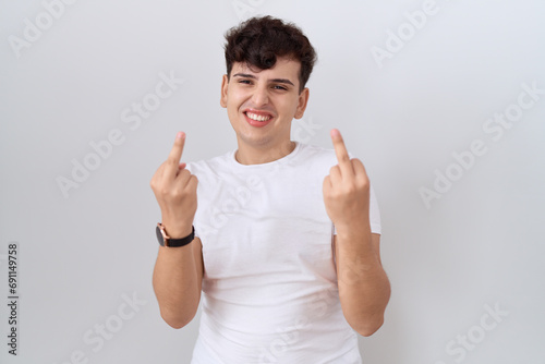Young non binary man wearing casual white t shirt showing middle finger doing fuck you bad expression  provocation and rude attitude. screaming excited