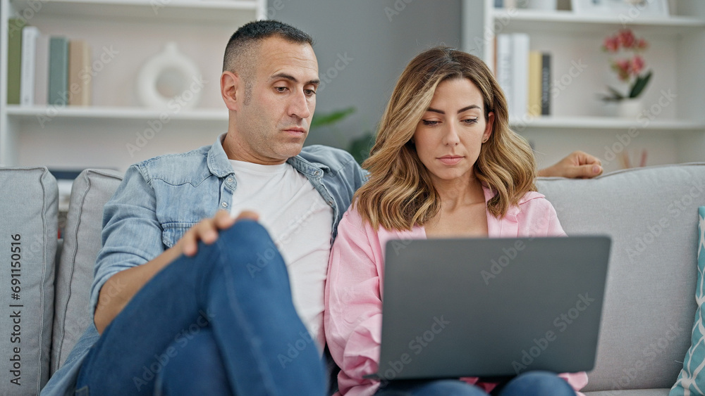 Man and woman couple using laptop sitting on sofa at home Man and woman couple using laptop sitting on sofa at home