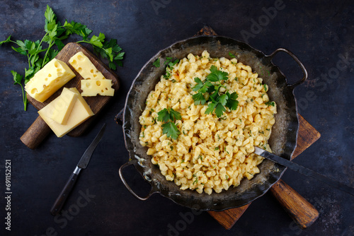 Traditional Allgäuer Käsespätzle with walnuts served as top view in a iron frying pan on a rustic wooden board at a mountain chalet photo