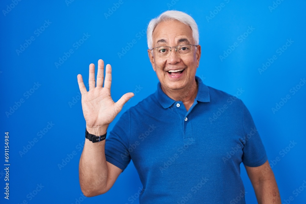 Middle age man with grey hair standing over blue background showing and pointing up with fingers number five while smiling confident and happy. Middle age man with grey hair standing over blue background showing and pointing up with fingers number five while smiling confident and happy.