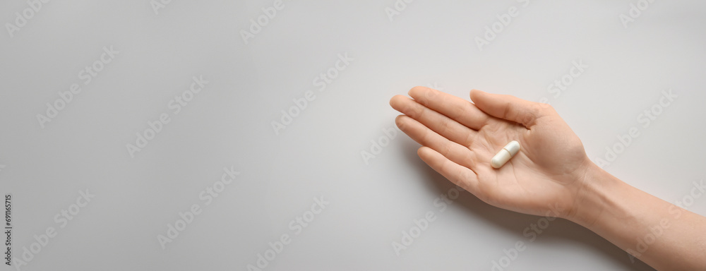 A single white capsule pill rests on the palm of a hand, displayed against a minimalist white background. Panorama with copy space. - obrazy, fototapety, plakaty 