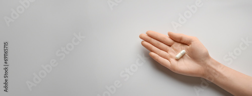 A single white capsule pill rests on the palm of a hand, displayed against a minimalist white background. Panorama with copy space. photo