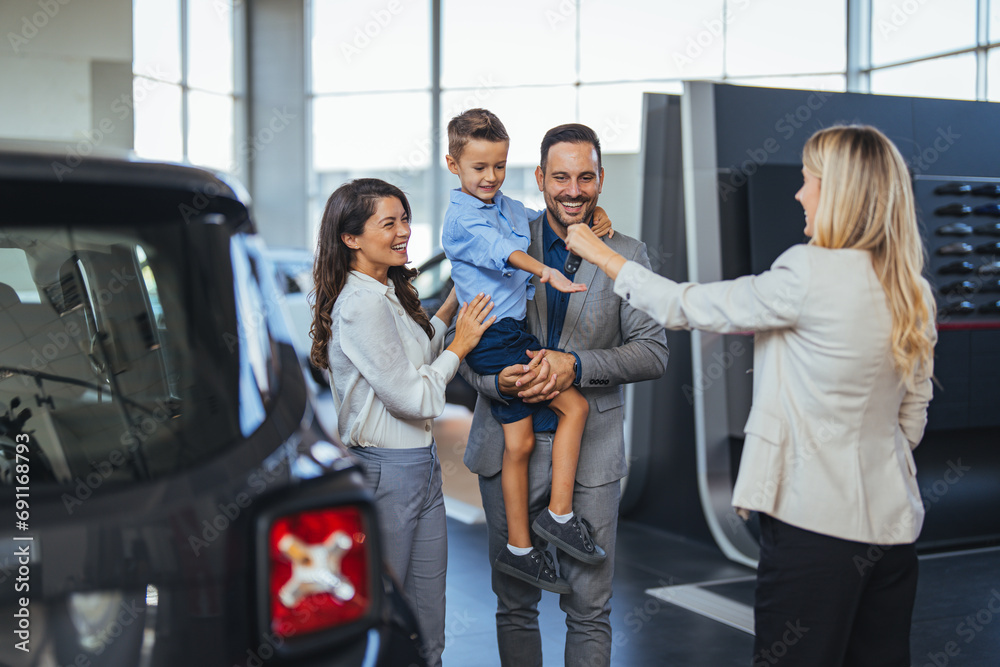 Happy family choosing new car, salesman showing them luxury auto at automobile dealership store. Customers selecting vehicle, consulting manager at modern showroom shop - obrazy, fototapety, plakaty 