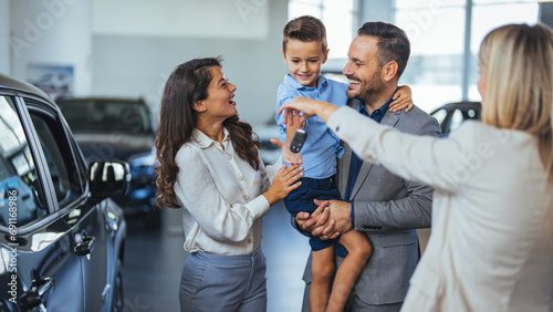 Young happy family and male salesperson using digital tablet in a car showroom. Happy young family buying their new car. 