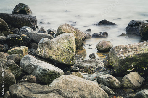 Cobblestones and rocks along the seacoast with smooth water through long exposure shot