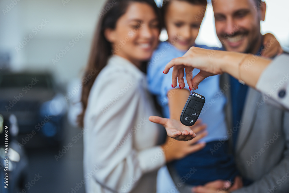 Happy family holding the keys of their new car at the dealership. Saleswoman at car dealership center helping family to choose new family vehicle.