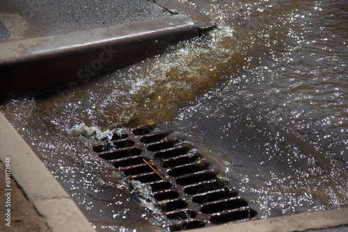 Flow of water during heavy rain and clogging of street sewage. The flow of water during a strong hurricane in storm sewers. Sewage storm system along the road to drain rain into the drainage system photo