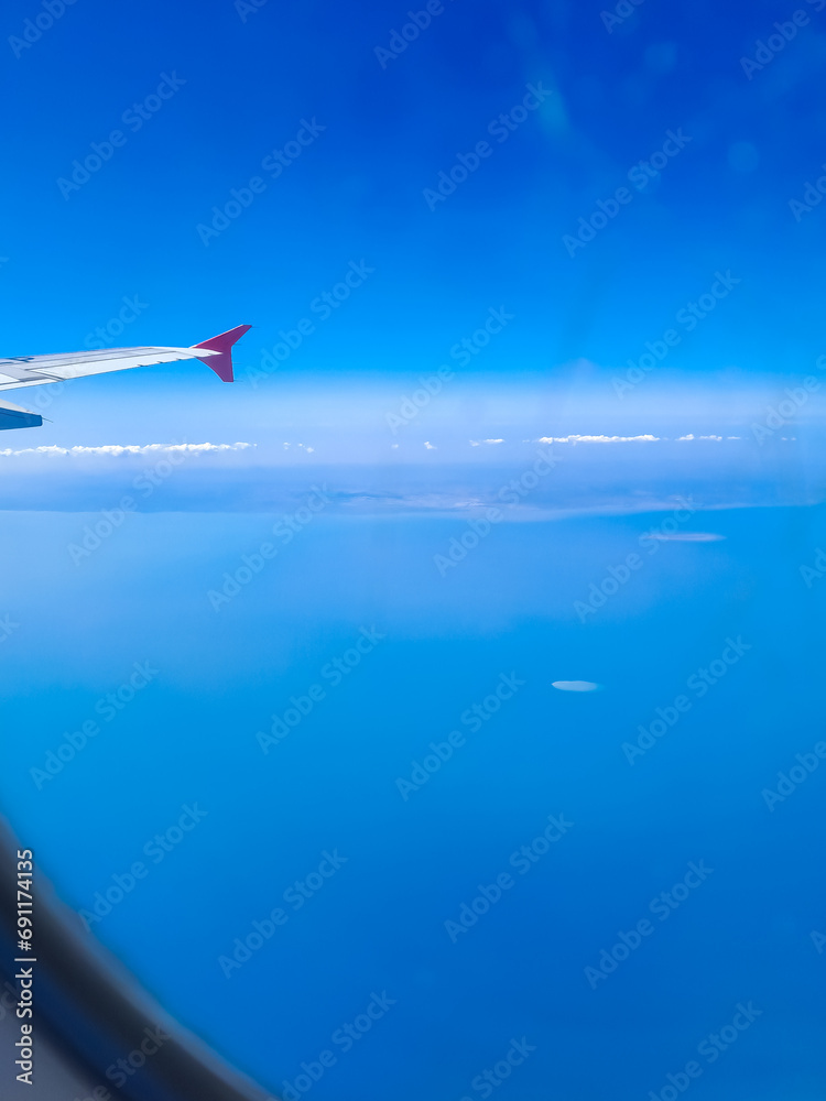 Airplane wing with clear blue sky and ocean behind, taken from passenger window Airplane wing with clear blue sky and ocean behind, taken from passenger window