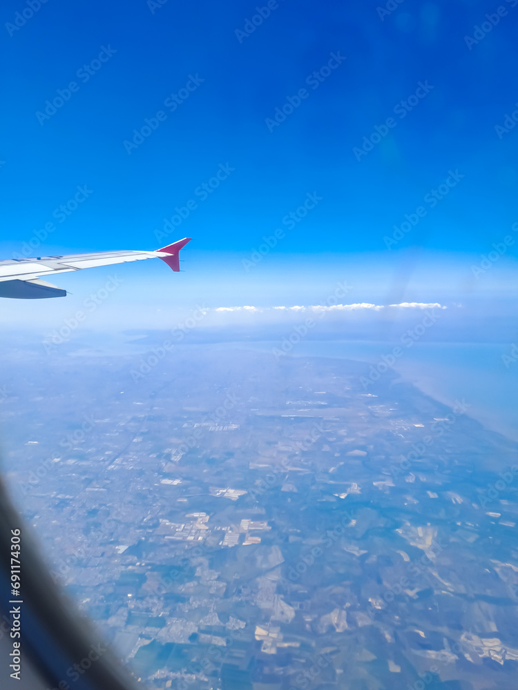 Fototapeta premium Airplane wing with clear blue sky and residential area behind, taken from passenger window