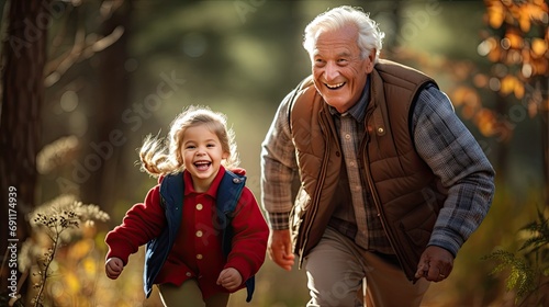 Joyful grandfather and granddaughter running together in sunlit autumn park.
