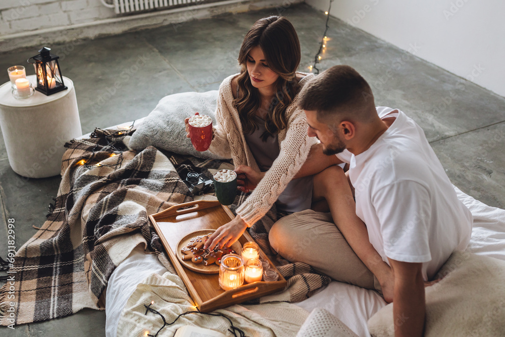 Concept of lazy weekend in bed or romantic home holiday celebration: christmas, new year, saint Valentine's Day. Beautiful young loving couple enjoy time together, embracing, kissing, having fun