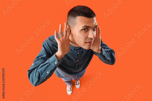 Young man with hearing problem on orange background photo