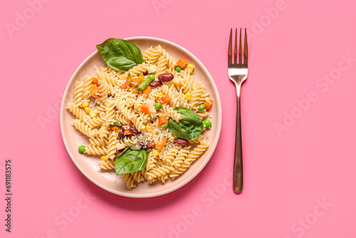 Plate with tasty pasta primavera on pink background