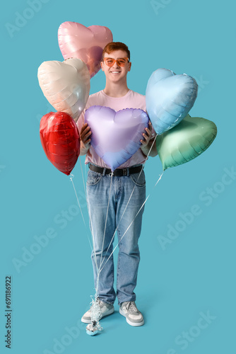 Happy young man with heart shaped air balloons on blue background