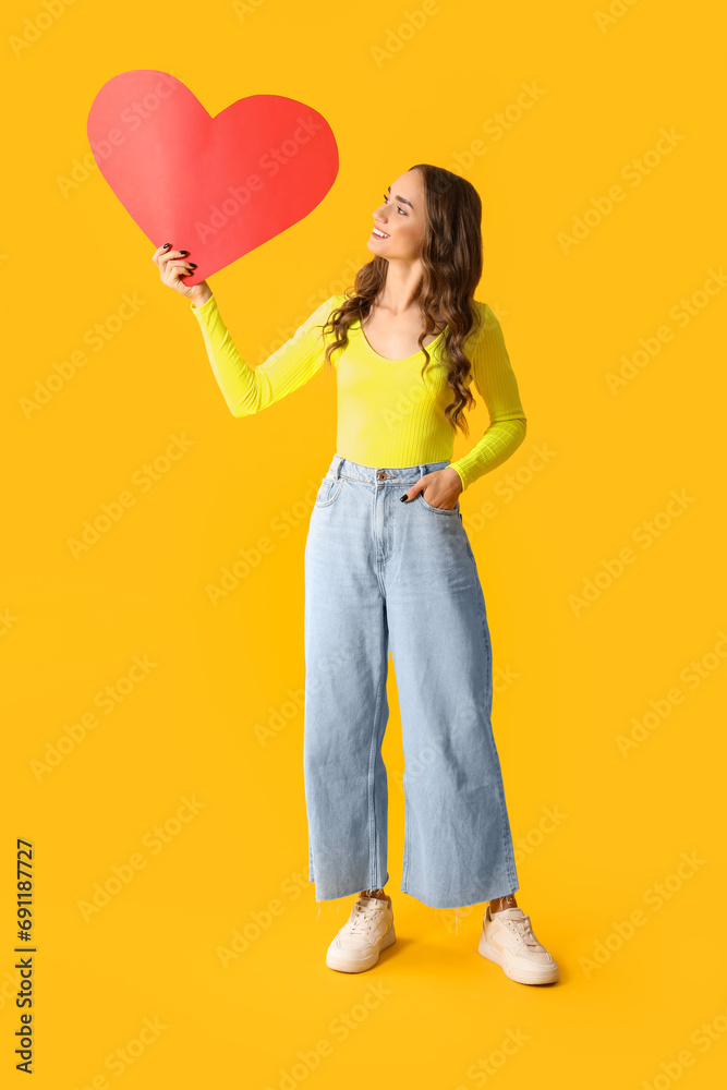 Beautiful young woman with red paper heart on yellow background Beautiful young woman with red paper heart on yellow background