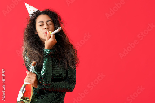 Beautiful young African-American woman with party whistle and bottle of champagne celebrating Birthday on red background photo