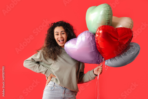 Beautiful young African-American woman with heart shaped air balloons on red background