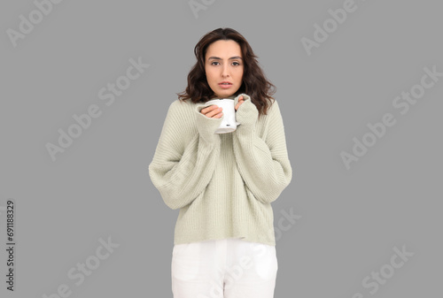 Sick young woman with cup of tea on grey background