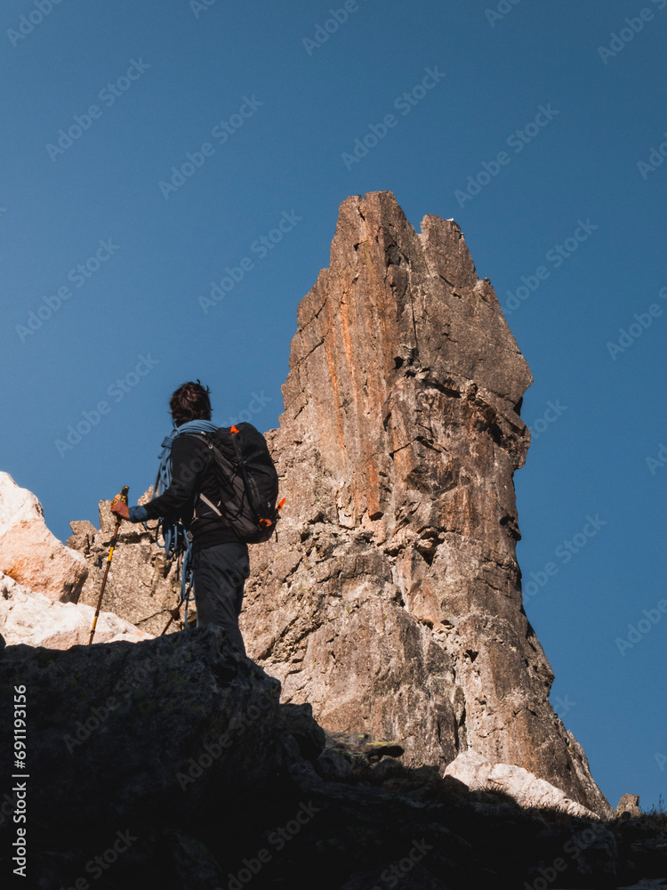 hiker with a backpack mountaineering in the Pyrenees in front of an imposing rock spire in summer