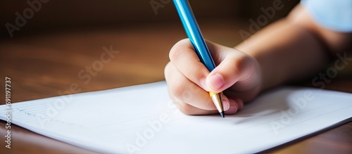 Closeup child do a handwriting homework of Chinese language on the desk focus at the left hand that hold the pencil. Copy space image. Place for adding text