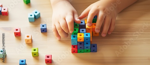 Childish male hands assembling trinomial cube wooden Montessori material on desk closeup top view Alternative education logical ecology construction for learning math algebra geometry arithmeti photo