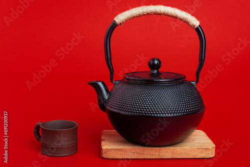 Traditional black Asian cast iron kettle teapot on wooden stand and clay cup on red background