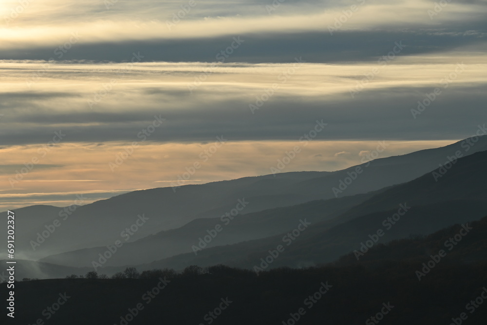 A view of a mountain range at sunset and some trees on the mountain slope