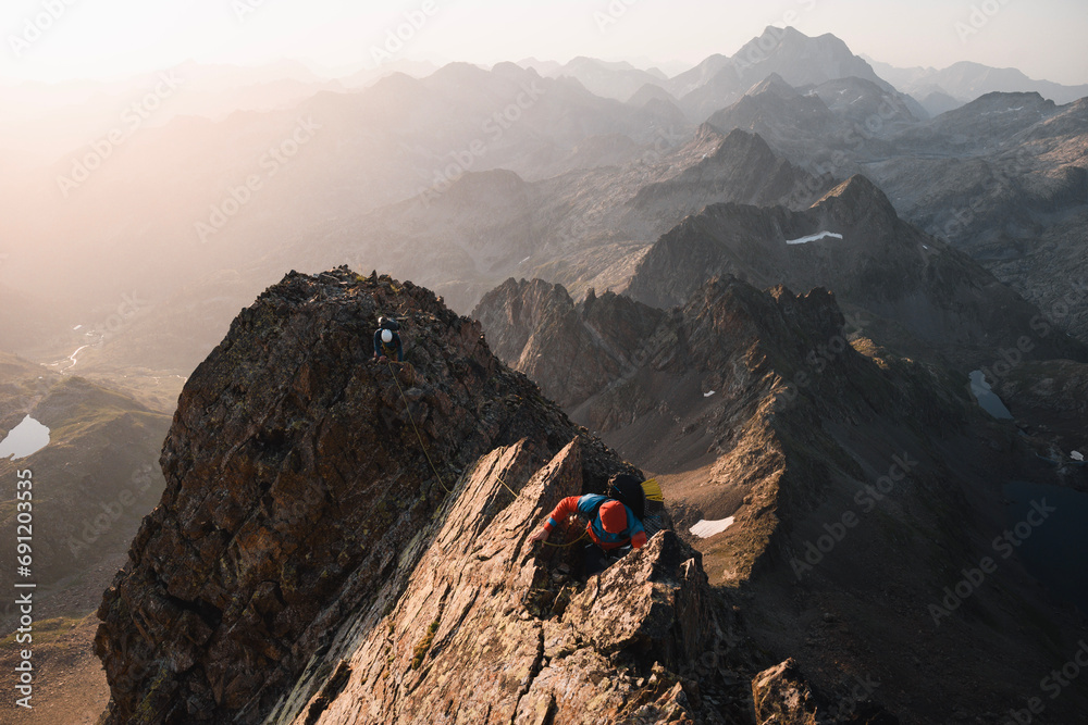 Two mountaineers climb roped together along a ridge of Pico Gran Facha in the Pyrenees at sunrise during the summer