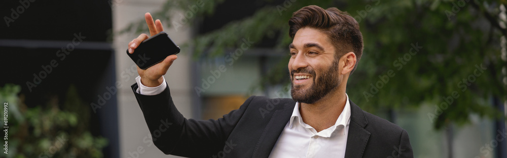 Smiling male manager standing near car with phone and waving hi to colleagues. High quality photo Smiling male manager standing near car with phone and waving hi to colleagues. High quality photo